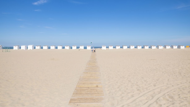 Une plage avec une promenade en bois qui mène à une rangée de cabanes de plage blanches et bleues.