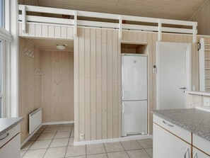 Une cuisine compacte dotée d’un réfrigérateur encastré, de murs recouverts de panneaux en bois et d’un petit plan de travail.
