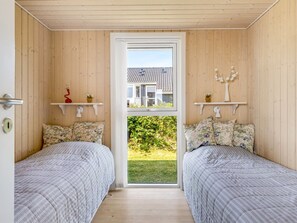 A room with two beds, wooden walls, a door leading outside, and a window with a view of a house and greenery. - "Finn" - 100m from the sea by Interhome (Sydals)
