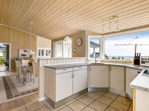 A modern kitchen with a large island, a dining area with chairs, and a view of the sea. - "Finn" - 100m from the sea by Interhome (Sydals)