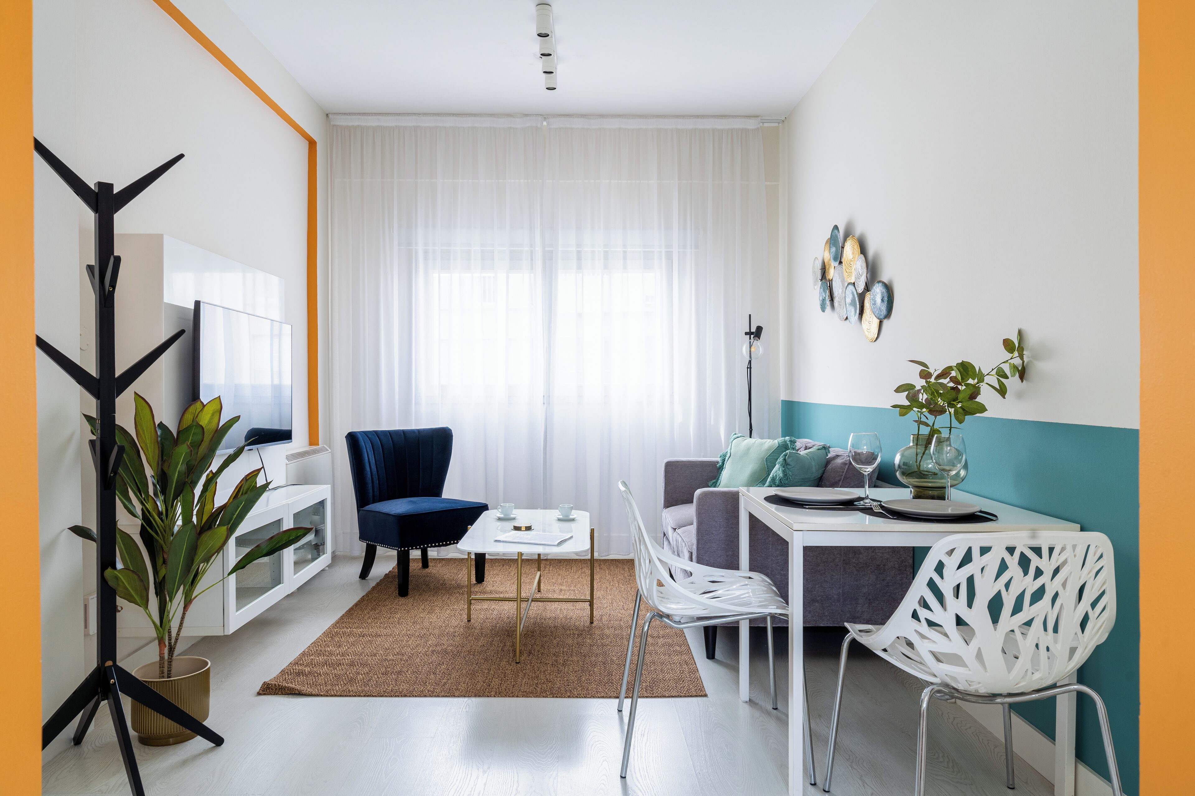 A modern living room with a sofa, a dining table with chairs, a coffee table, a potted plant, and a television.