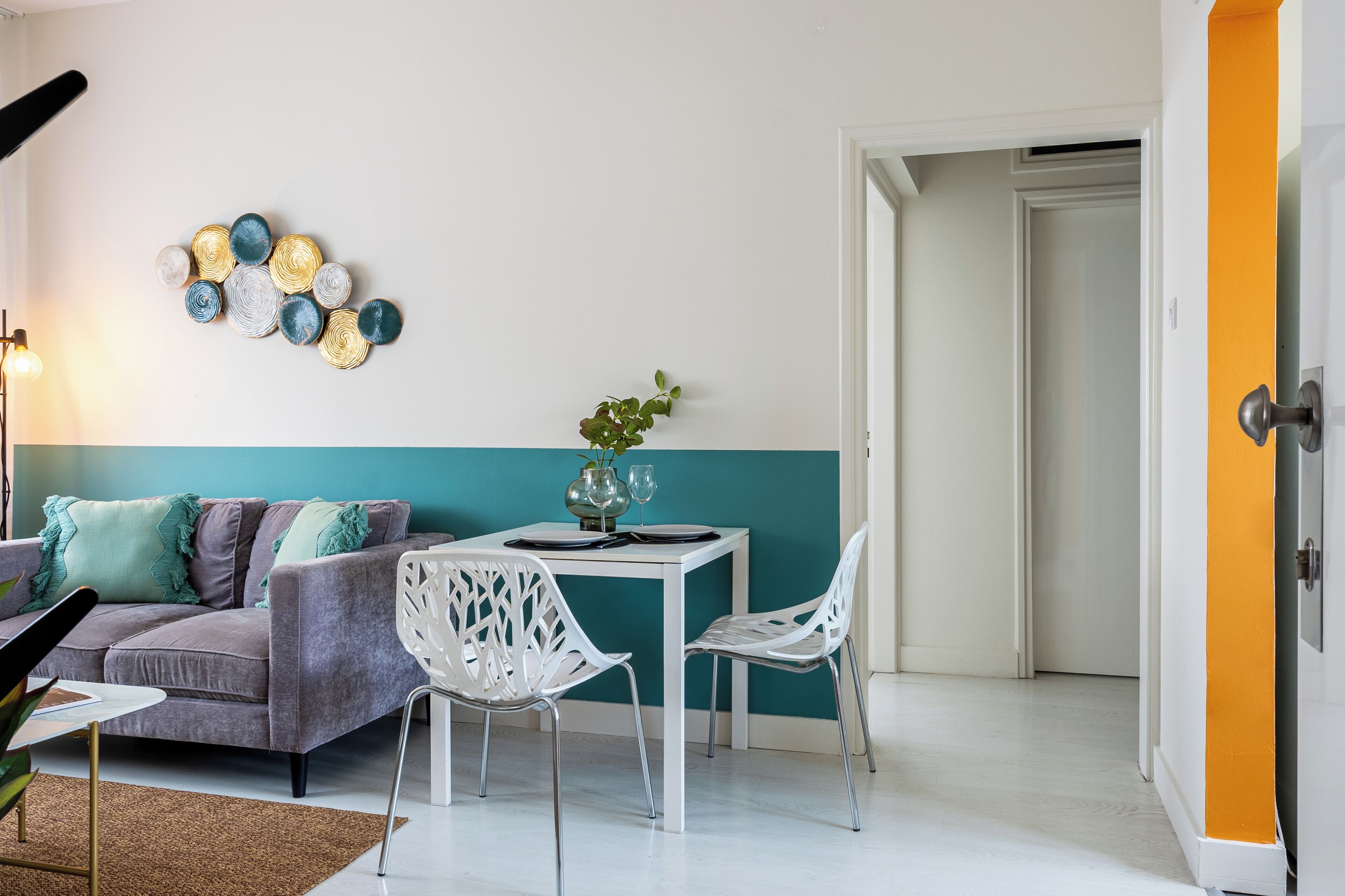 Una sala de estar moderna con un sofá gris, sillas blancas, una pared de acento color turquesa y un elemento decorativo en la pared.