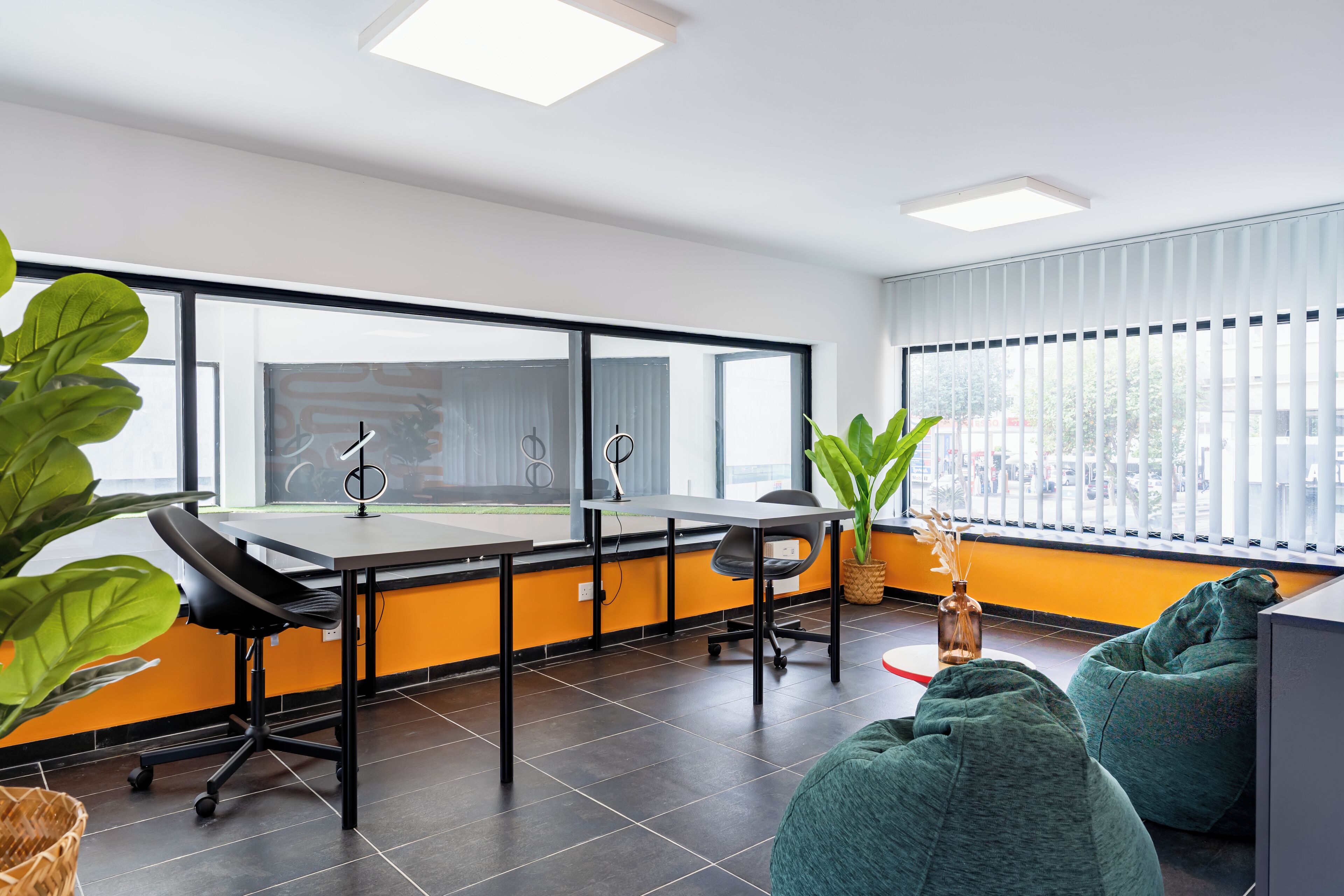 A modern office space with a large window, two desks, chairs, and green bean bag chairs.