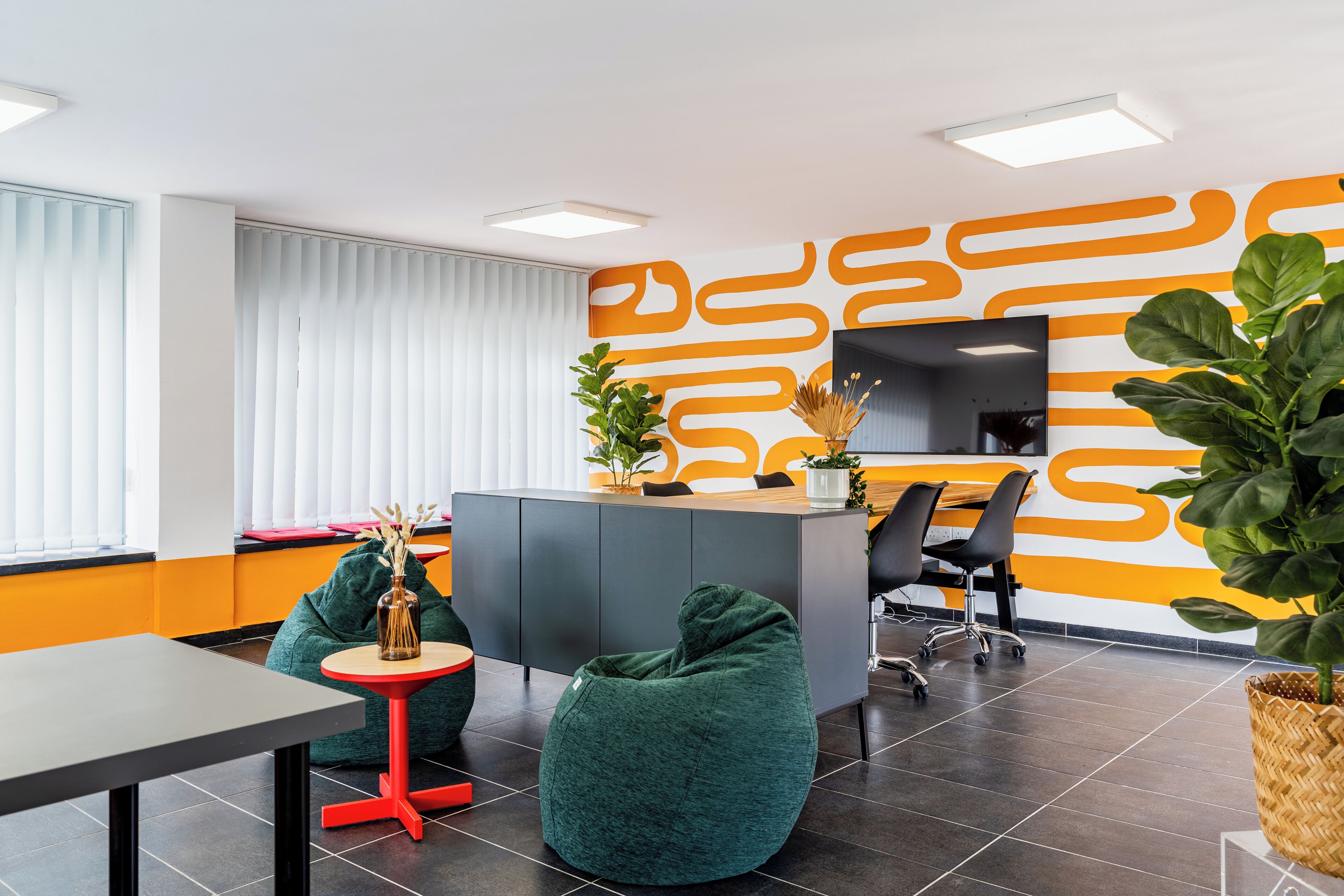 A modern office space with a reception desk, green bean bag chairs, a small table, and a large potted plant.