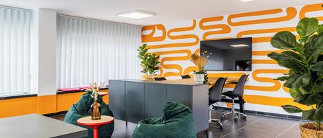 A modern office space with a reception desk, green bean bag chairs, a small table, and a large potted plant.