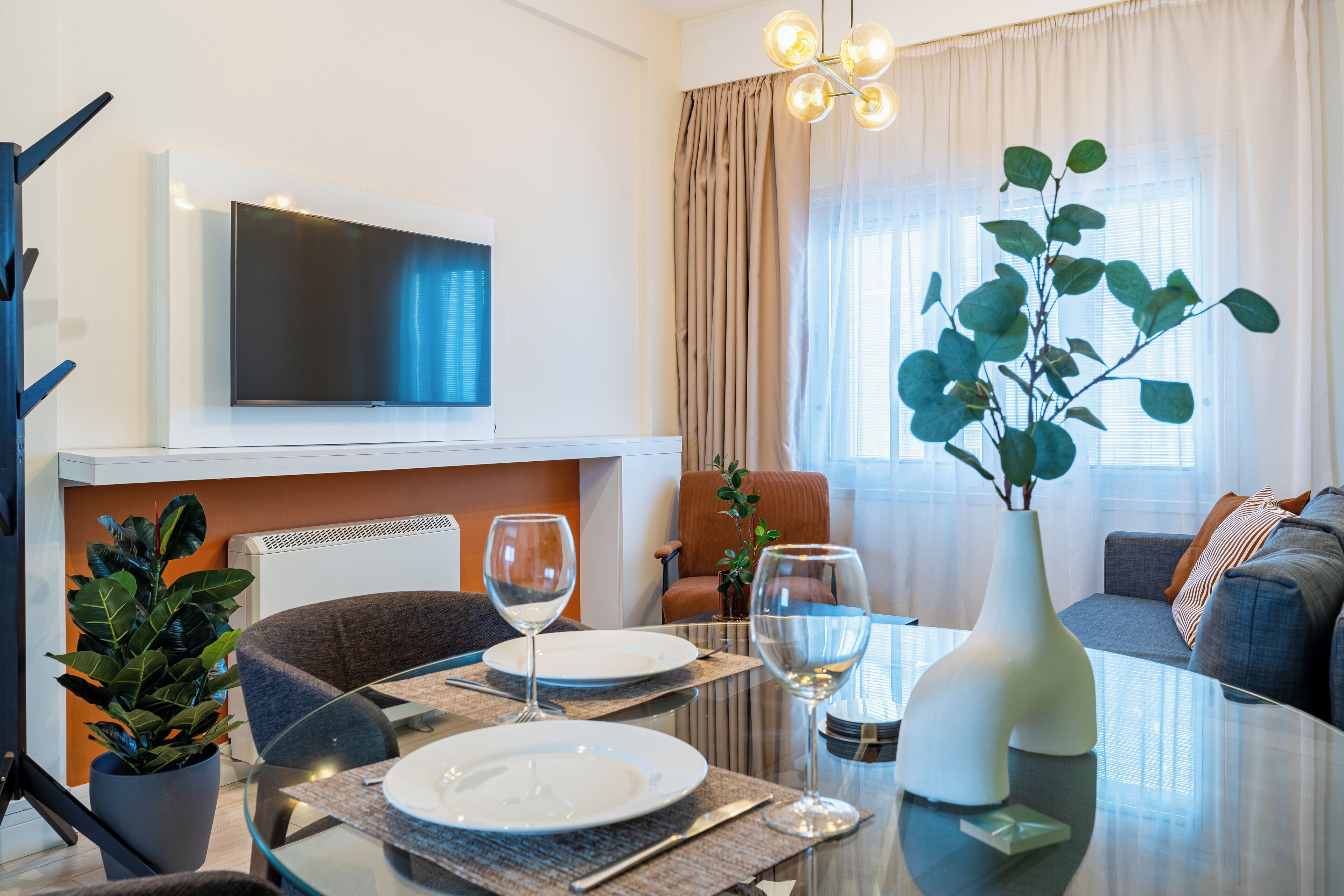 Una sala moderna con una mesa de vidrio, un televisor de pantalla plana en la pared, un sofá y una planta en maceta.