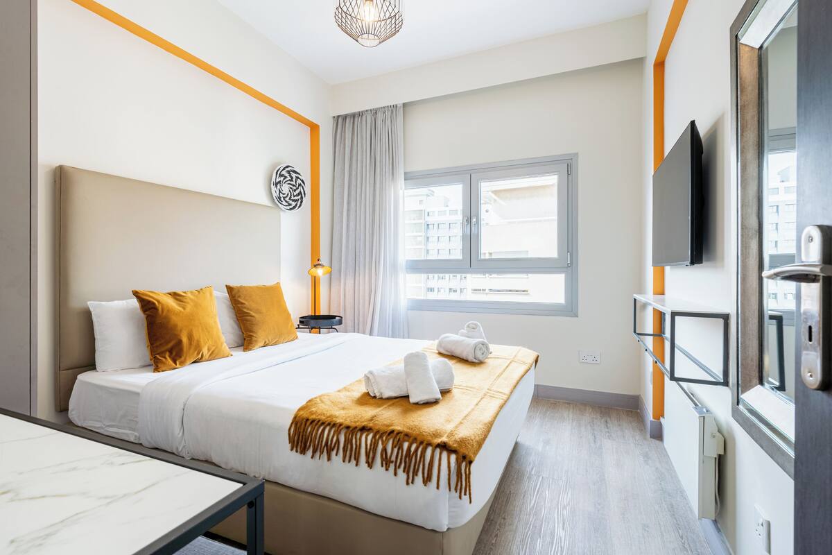 A modern hotel room with a bed, bedside table, and a large window.