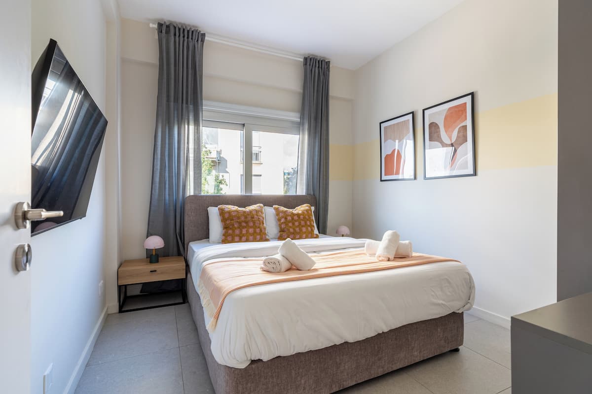 A modern hotel room with a large bed, a flat-screen TV mounted on the wall, and two framed artworks on the wall.