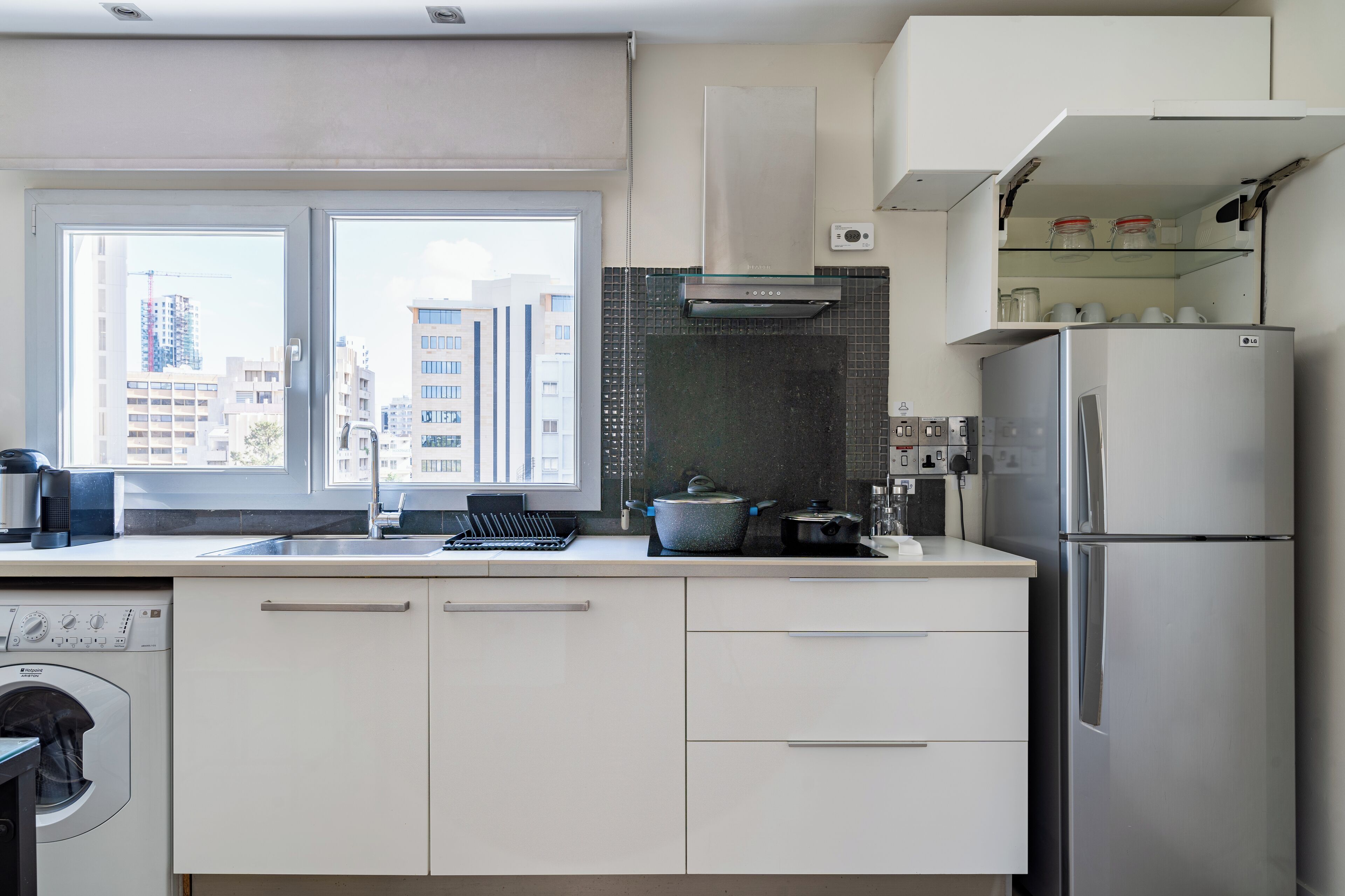 A modern kitchen with a built-in washing machine, a stainless steel refrigerator, and a window with a city view.