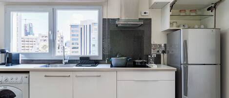 A modern kitchen with a built-in washing machine, a stainless steel refrigerator, and a window with a city view.