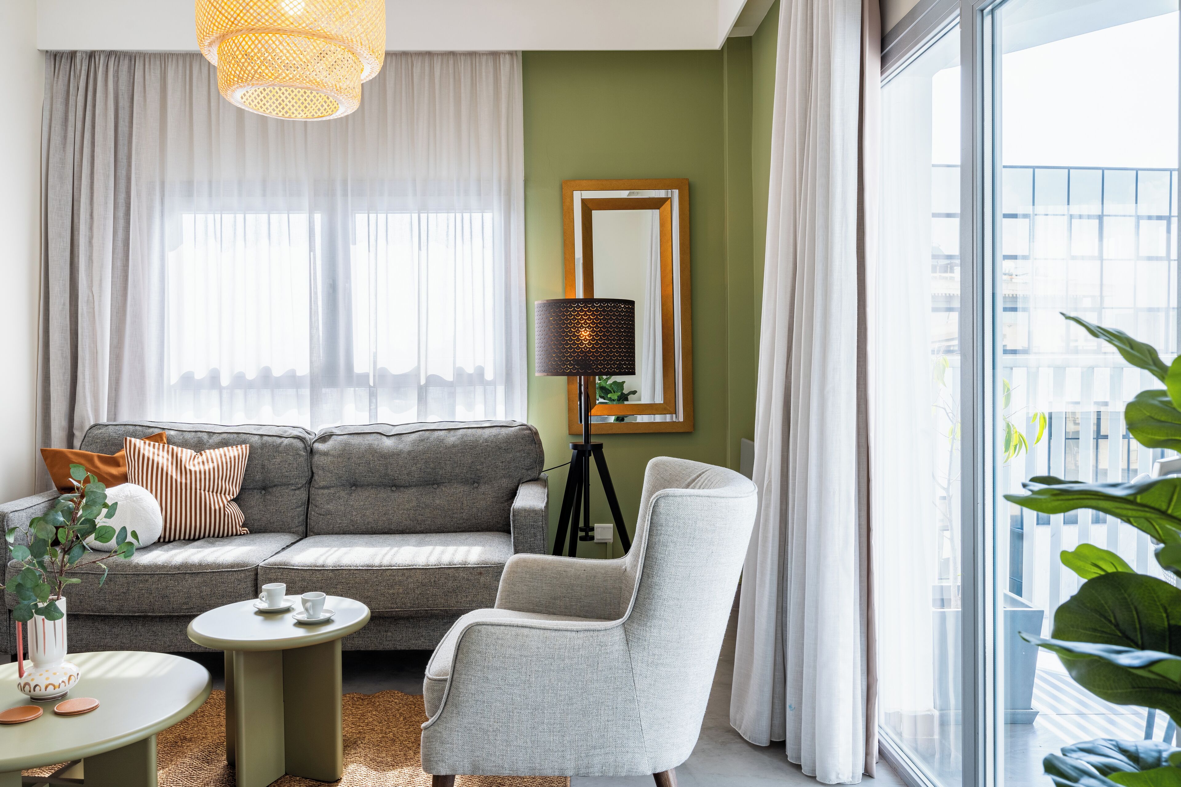 A modern living room with a grey sofa, a round coffee table, and a grey armchair. A floor lamp and a mirror are on the wall.