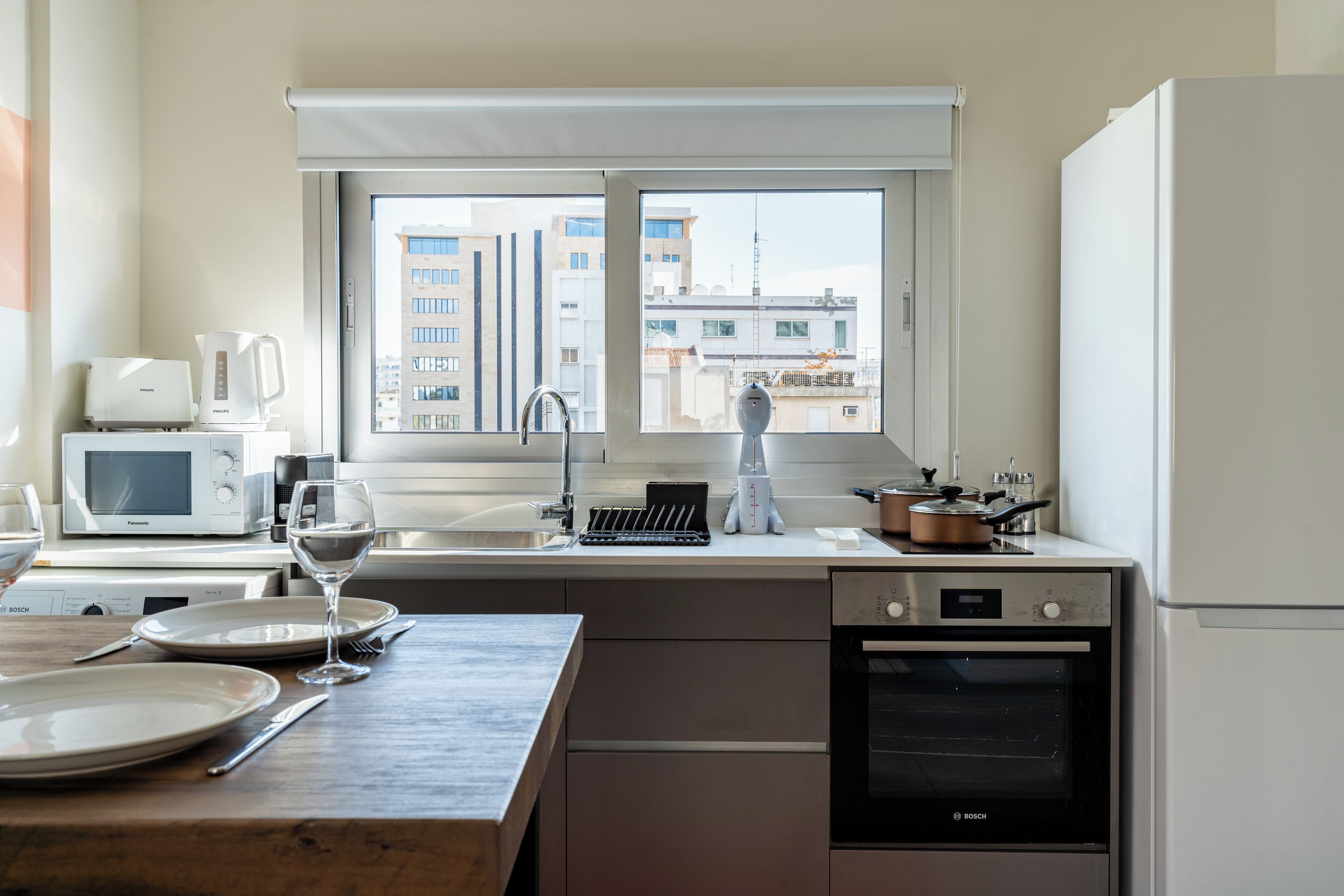 Cocina moderna con horno Bosch, microondas y cafetera. Se aprecia una ventana con vistas a edificios.