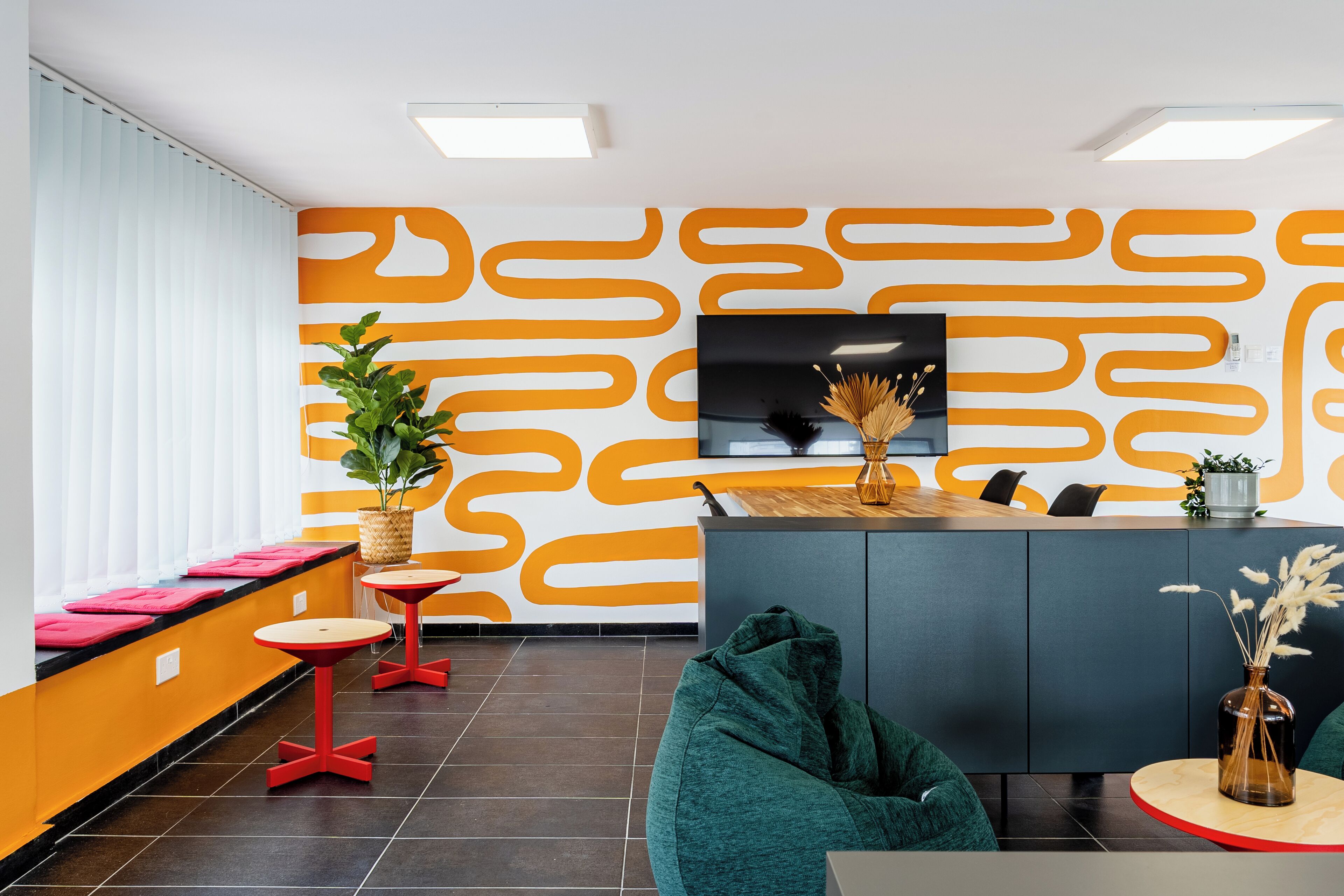 A modern reception area with a patterned wall, a TV, seating, and a plant.