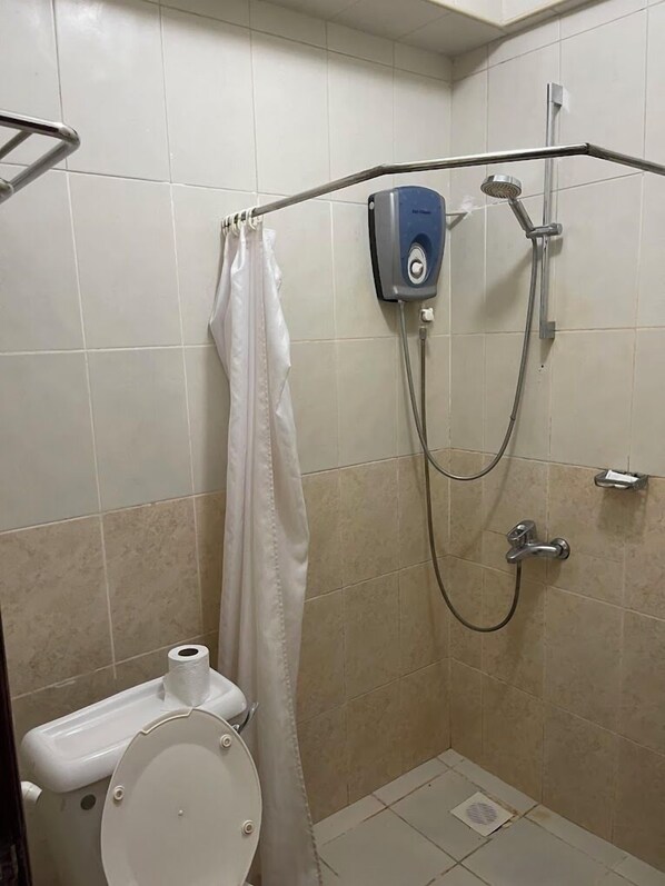 A small, tiled bathroom with a shower, toilet, and a towel rack.