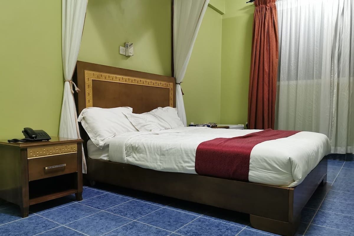 Una habitación de hotel con una cama, una mesita de noche con un teléfono y una lámpara fijada en la pared.