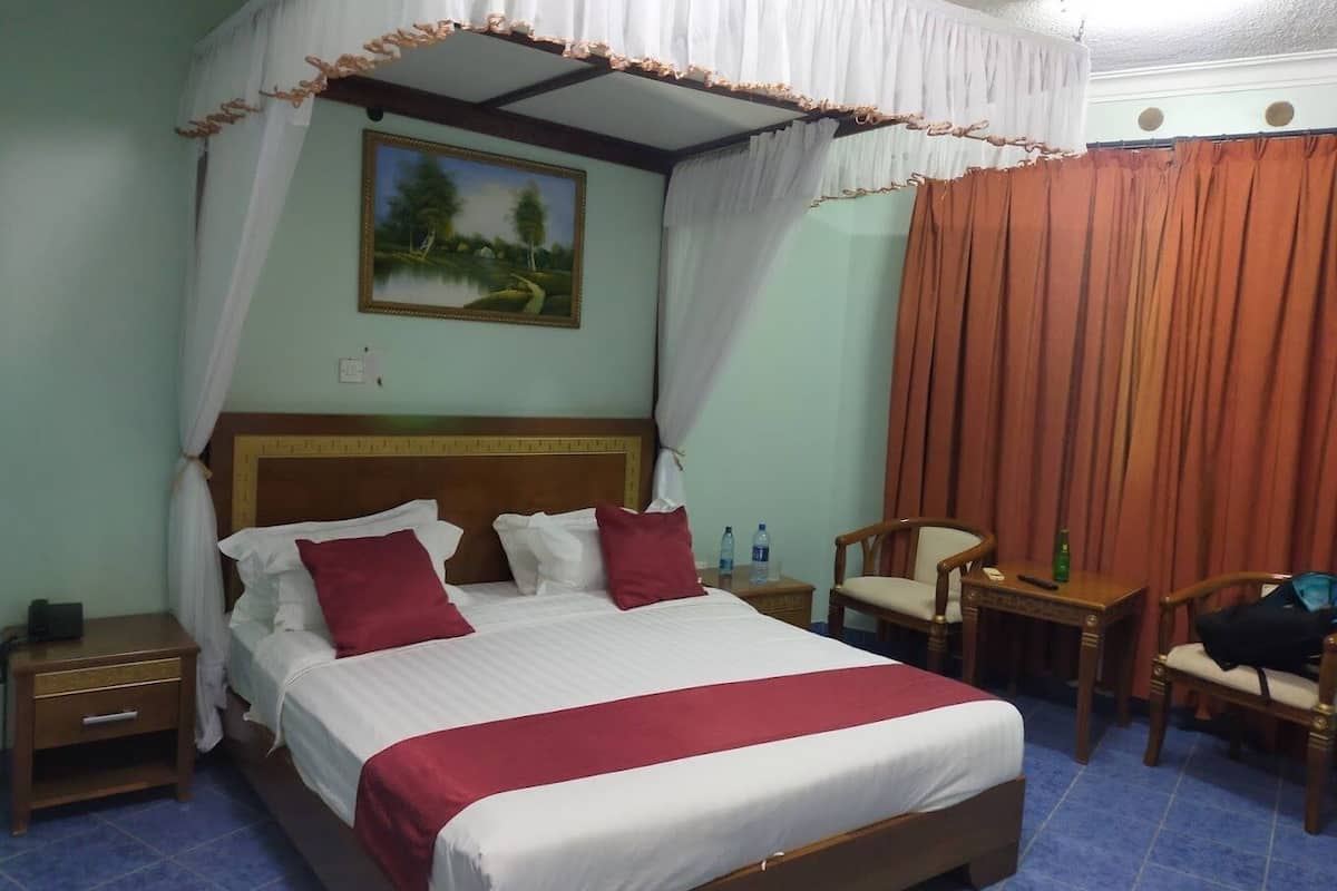 Habitación de hotel con cama con dosel, mesita de noche, una silla y una pequeña mesa con una botella y un control remoto.