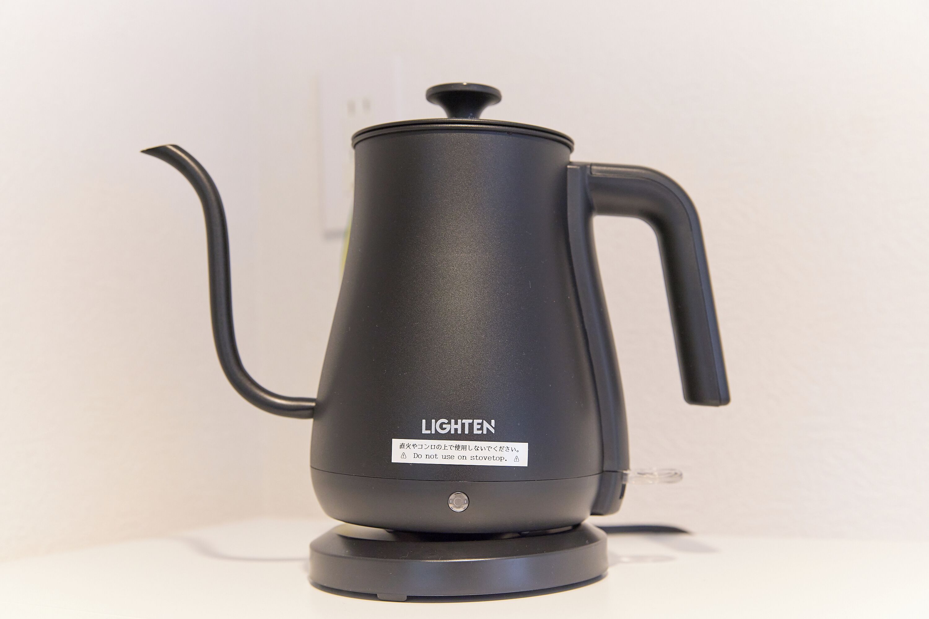 En svart, elektrisk vattenkokare med handtag och pip, märkt med texten ”LIGHTEN”, placerad på en vit yta.