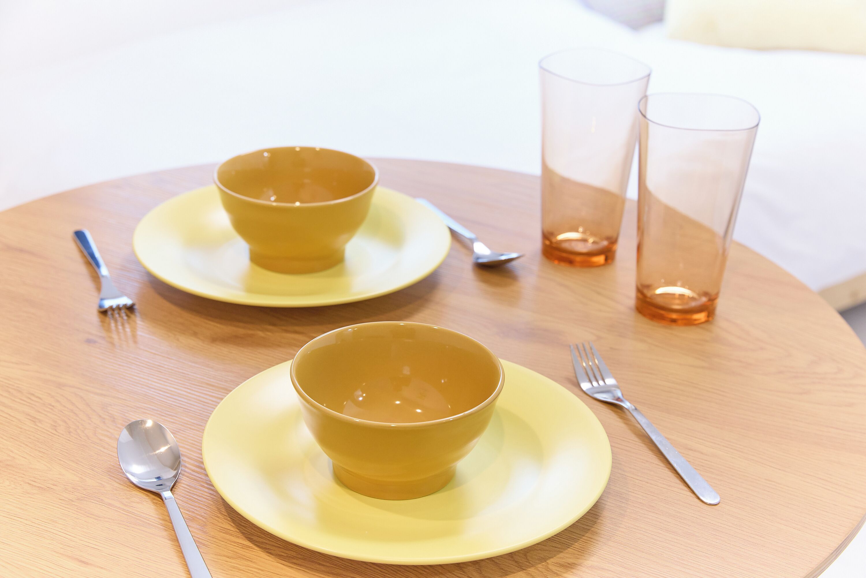 Une table à manger avec deux bols jaunes, deux verres transparents et des couverts.