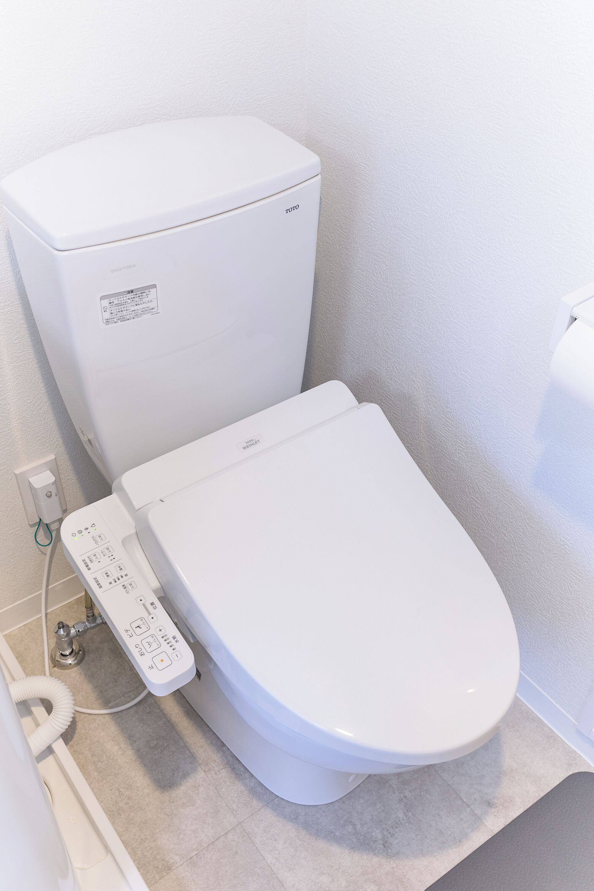 A modern toilet with a control panel, a white wall, and a tiled floor.