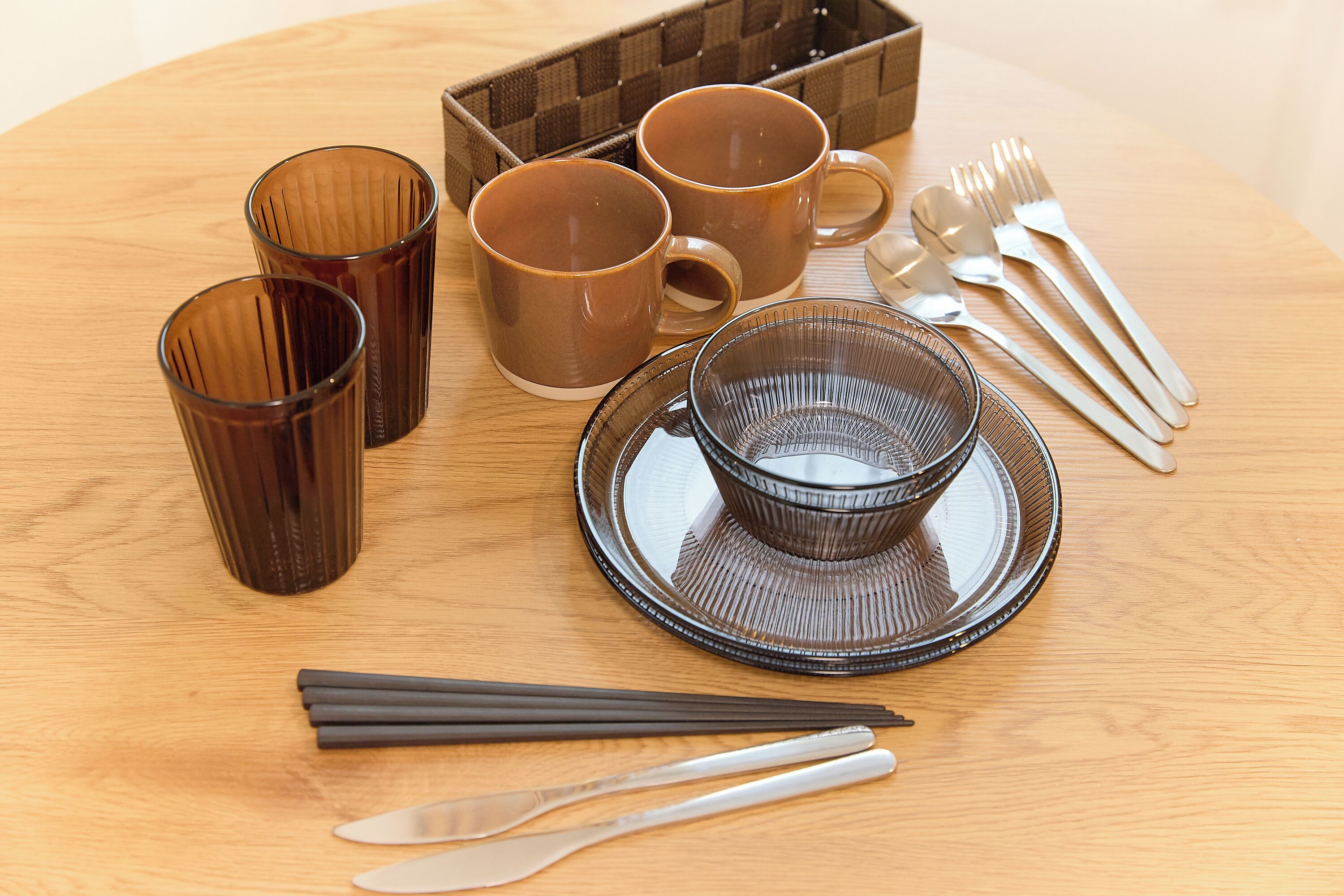 A table setting with brown cups, a bowl, chopsticks, and cutlery.