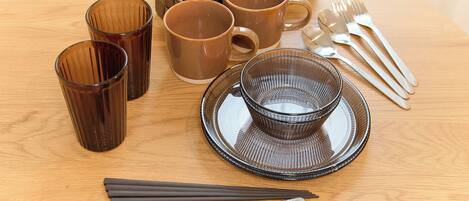 A table setting with brown cups, a bowl, chopsticks, and cutlery.