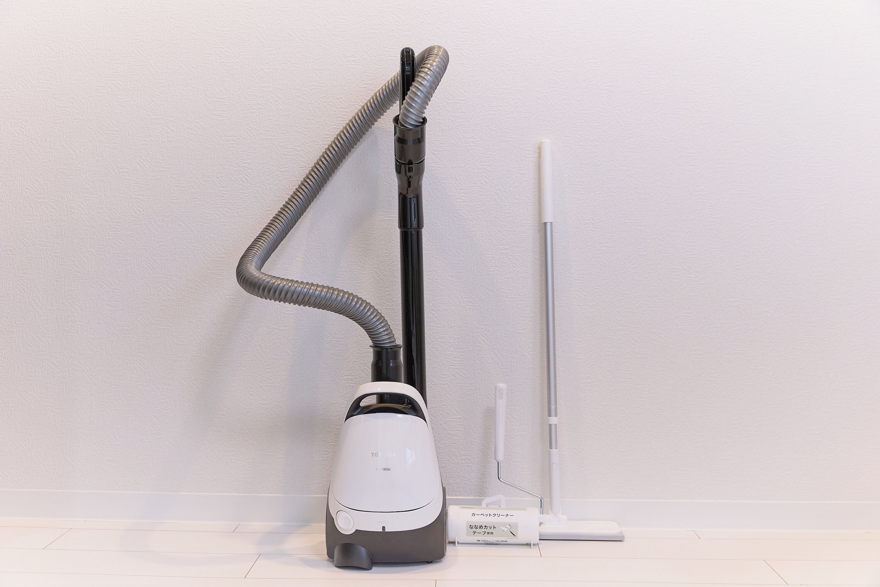 A vacuum cleaner with a hose and a canister, placed against a white wall.