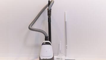 A vacuum cleaner with a hose and a canister, placed against a white wall.