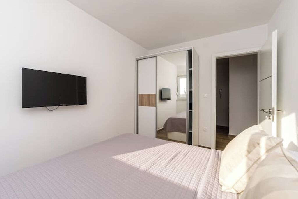 Ein Schlafzimmer mit einem Bett, einem an der Wand befestigten Fernseher und einer Schiebetür zu einem anderen Raum.