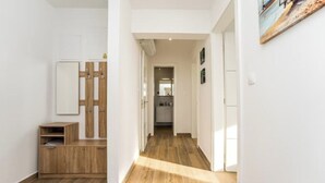 A hallway with wooden flooring, a wooden cabinet, a mirror, and a door leading to a kitchen area. - Apartment 3 (Novalja)