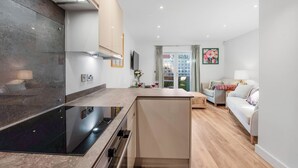 Una cocina moderna con estufa integrada, un comedor con mesa y sillas, y una sala de estar con sofá y televisor.