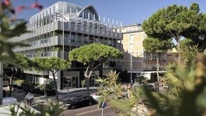 A modern building with a curved glass facade, surrounded by trees and a parking area. - Vespucci Home – Elegance (Rimini)