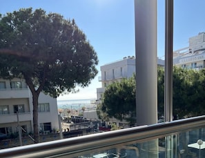 Vista des del balcó sobre una zona costanera amb edificis, un arbre i un cel serè.
