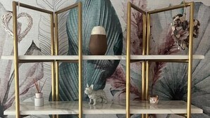 A room with a decorative wall featuring leaf patterns and a gold-framed shelving unit with white marble shelves. - Vespucci Home – Elegance (Rimini)
