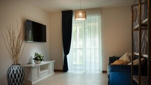 A modern living room with a flat-screen TV, a large vase, a blue sofa, and a bookshelf. - Vespucci Home – Elegance (Rimini)