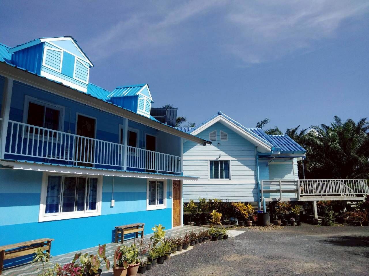 A two-story building with a blue and white exterior, a balcony on the upper floor, and a small porch area with potted plants.