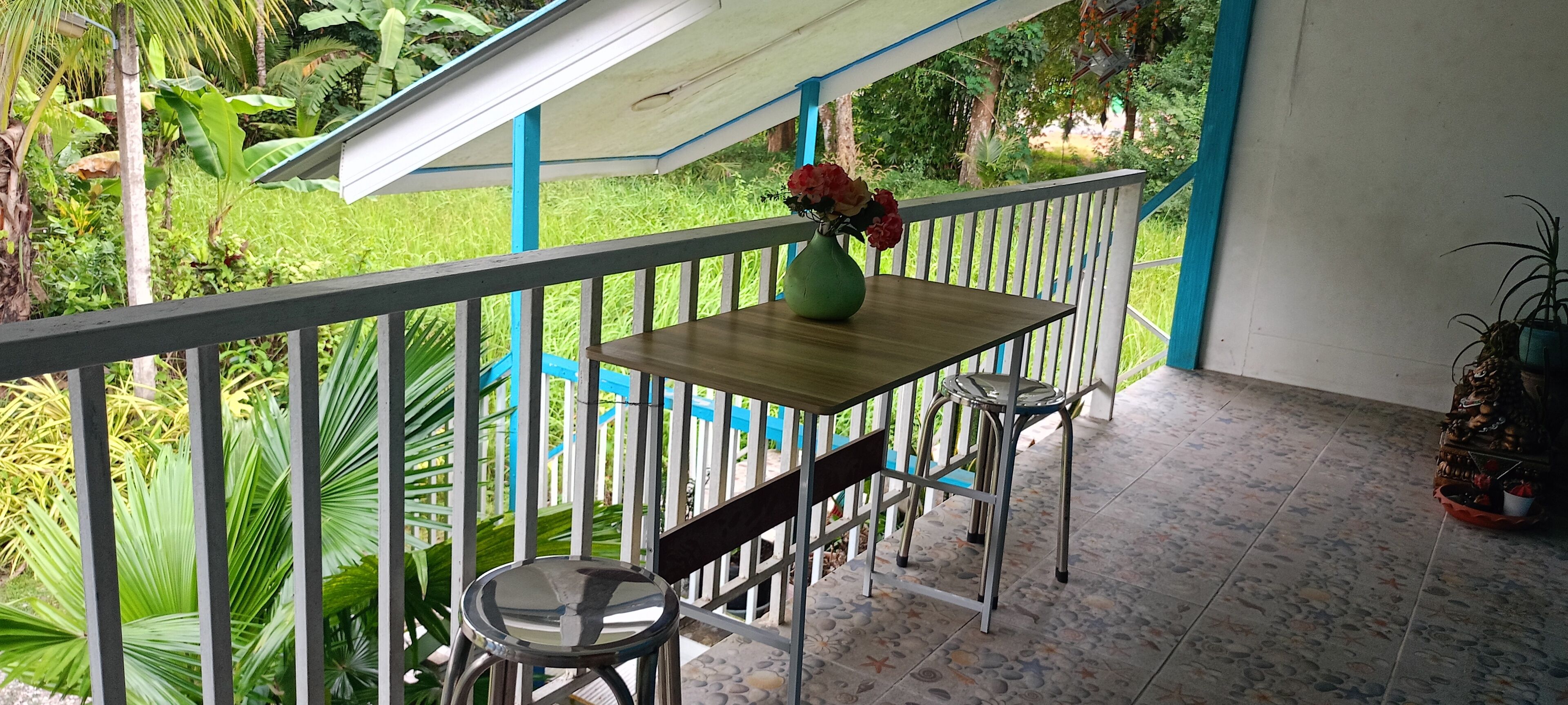A balcony with a wooden table and two chairs, a green vase with flowers, and a potted plant.