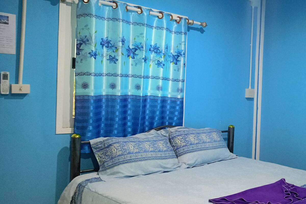 A bedroom with a bed, a blue curtain, and three paintings on the wall.