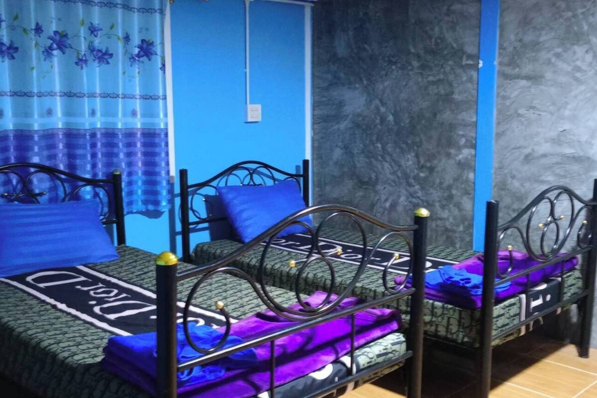 A room with two beds, each with a blue and purple bedspread, and a blue curtain with floral patterns.