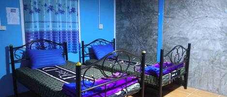 Una habitación con dos camas, cada una con una colcha azul y morada, y una cortina azul con motivos florales.