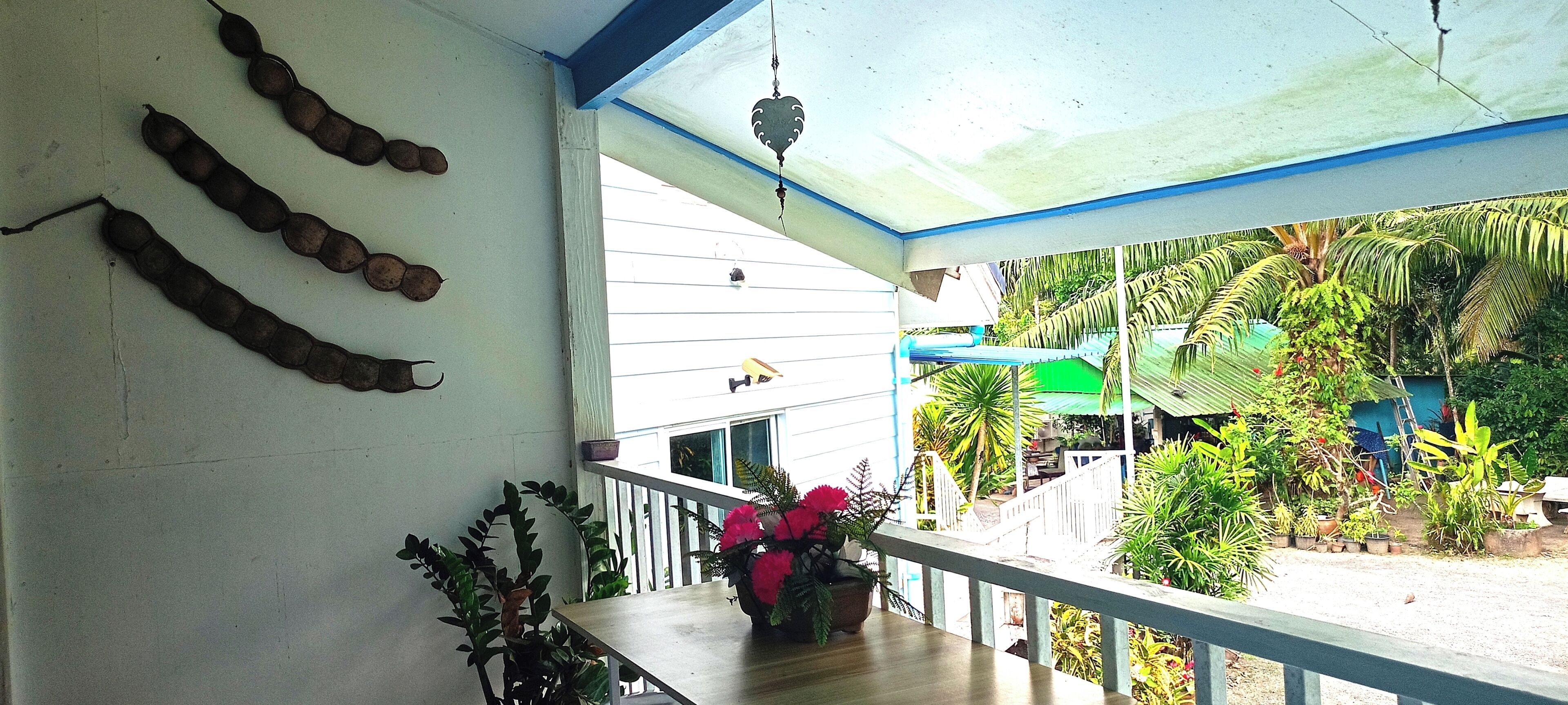 A balcony with a view of a garden, a hanging ornament, and a wooden table with a potted plant.