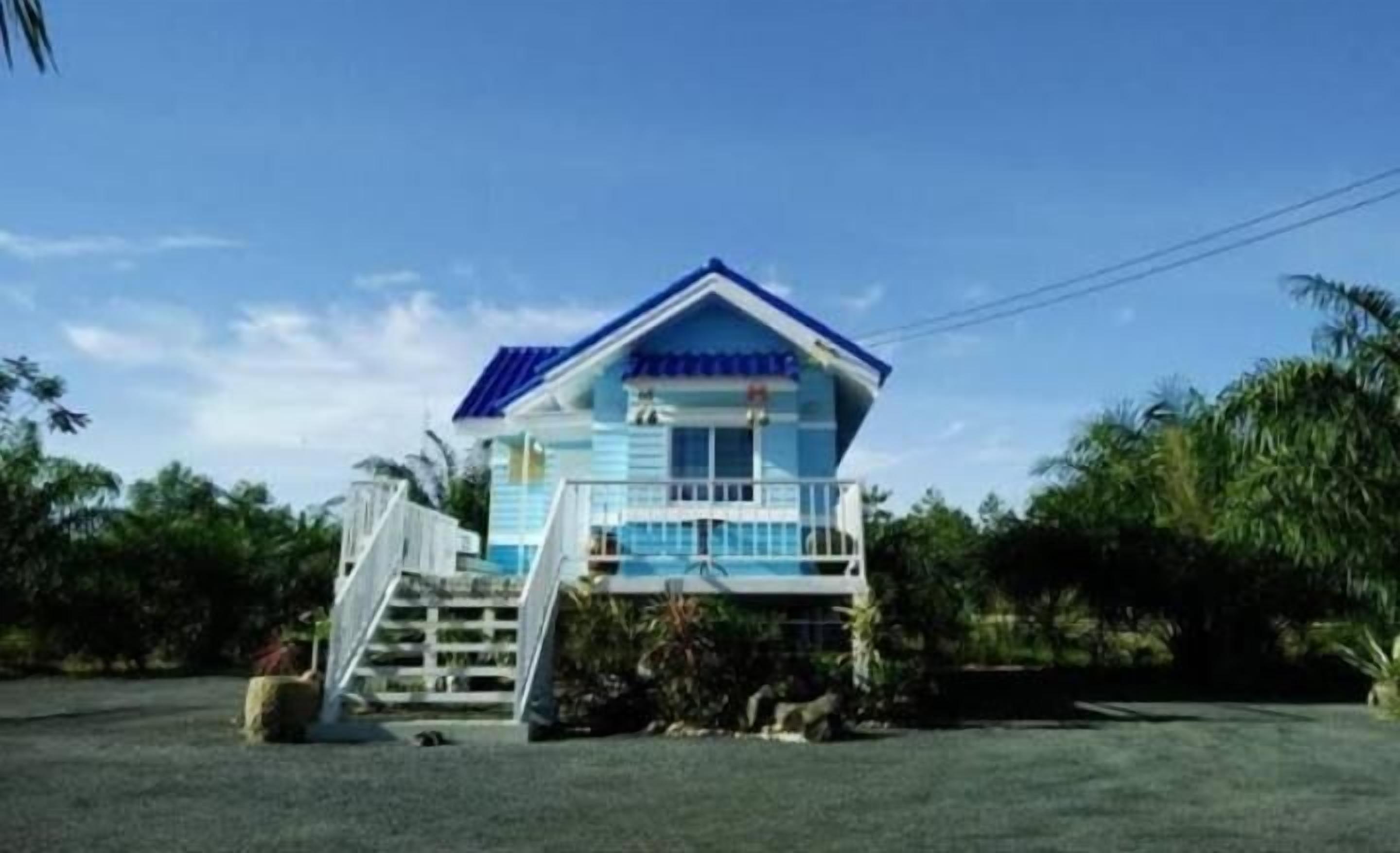A two-story building with a blue roof and white exterior, featuring a balcony and a staircase leading to the entrance.