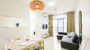 A modern living room with a grey sofa, a dining table set with plates and glasses, a large window with curtains, and a hanging light fixture. - Vista Sentul Residences by Airhost (Kuala Lumpur)
