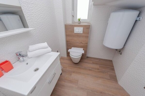 Ein modernes Badezimmer mit Waschbecken, Toilette und Dusche – alles in Weiß.