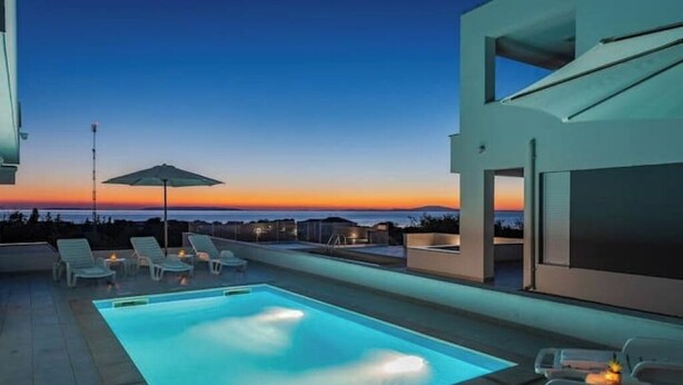 Un área de piscina moderna al aire libre con sillones de descanso y vista al atardecer.