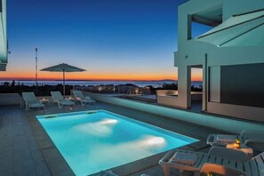 Ein moderner Poolbereich im Freien mit Liegestühlen und Blick auf den Sonnenuntergang.