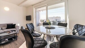 Una sala moderna con una mesa de comedor de vidrio, sillas de cuero negro, un sofá y un televisor montado en la pared.