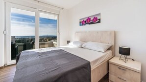 Un dormitorio con una cama grande, una mesita de noche y vistas de la ciudad a través de una puerta corrediza de vidrio.