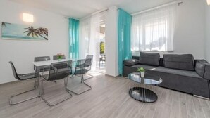 Una sala de estar moderna con un sofá gris, una mesa de centro de vidrio y un comedor con mesa y sillas blancas.