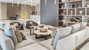 A modern lobby with a seating area, marble reception desk, and a bookshelf with travel books. - Luxury Suite Canal Views Infinity Pool (Dubai)