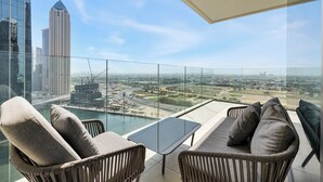 A balcony with wicker furniture, a glass table, and a view of a cityscape and construction site. - Luxury Suite Canal Views Infinity Pool (Dubai)